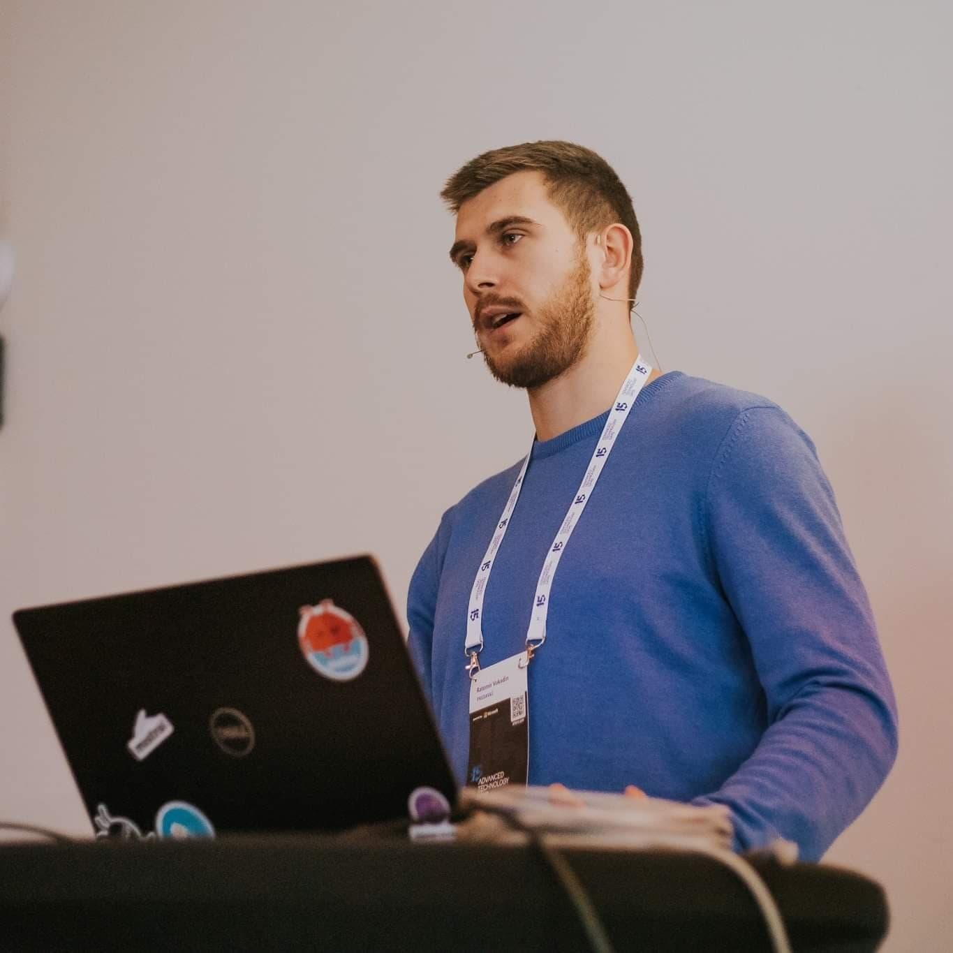 Ratomir Vukadin speaking at a conference beside an open laptop.